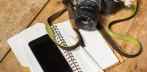 Photo of a note pad, pen, and camera on a wooden table illustrate the nonprofit story collecting tool.