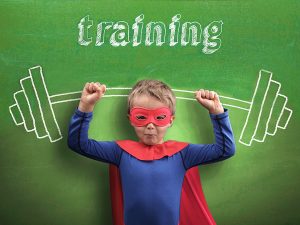 Boy in superman costume posing in front of chalkboard with image of huge barbell as illustration of nonprofit communications training